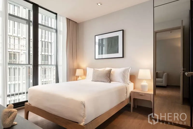 Condominium for rent in Khlong Toei, Bangkok - Cozy bedroom with bedside lamps, artwork, and tall windows with curtains.