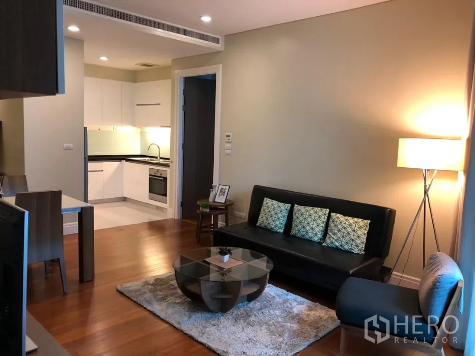 公寓 出租或出售在Khlong Toei, Bangkok - 开放式客厅，木地板，黑色皮沙发与玻璃圆几，连通白色L型厨房。