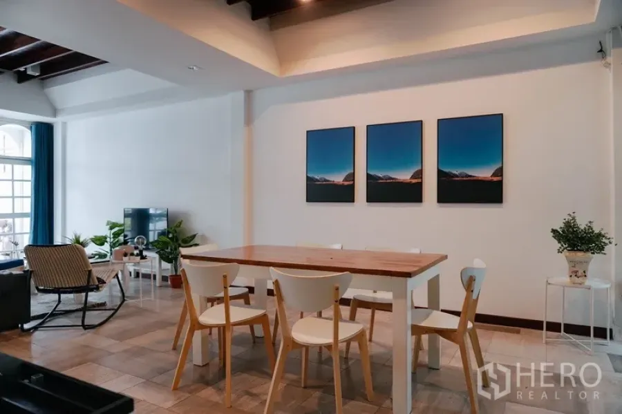 Townhouse for rent in Watthana, Bangkok - Open-plan dining and living area with wooden table, TV corner, wall art and indoor plants in a modern Bangkok townhouse.