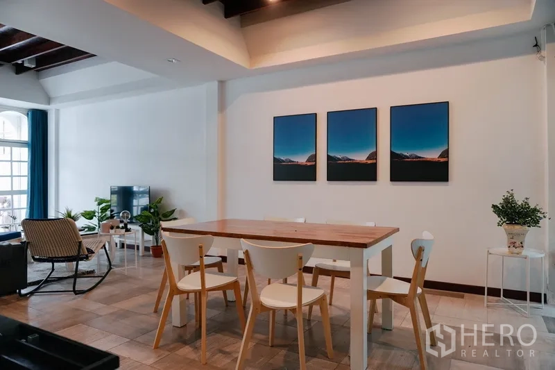 Townhouse for rent in Watthana, Bangkok - Open-plan dining and living area with wooden table, TV corner, wall art and indoor plants in a modern Bangkok townhouse.