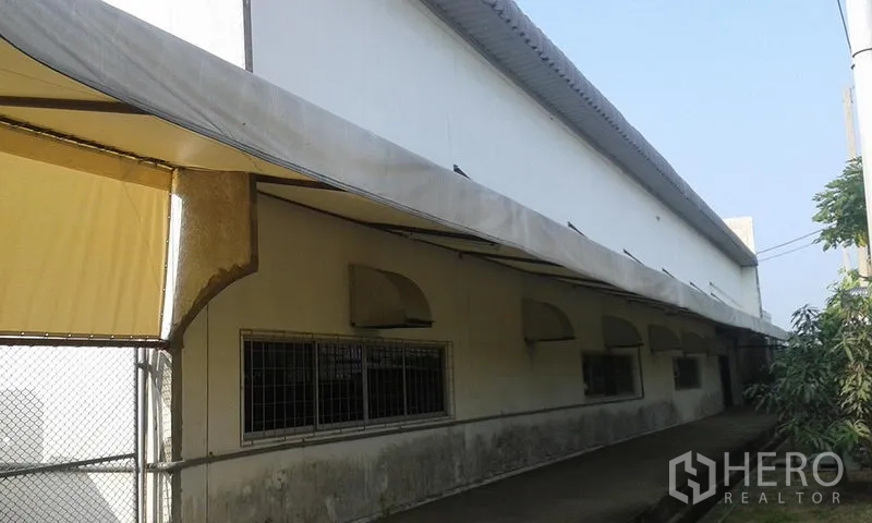 工厂 出租在Uthai, Phra Nakhon Si Ayutthaya - 工厂侧边走道，长条遮阳篷、带护栏窗户及铁丝网大门。