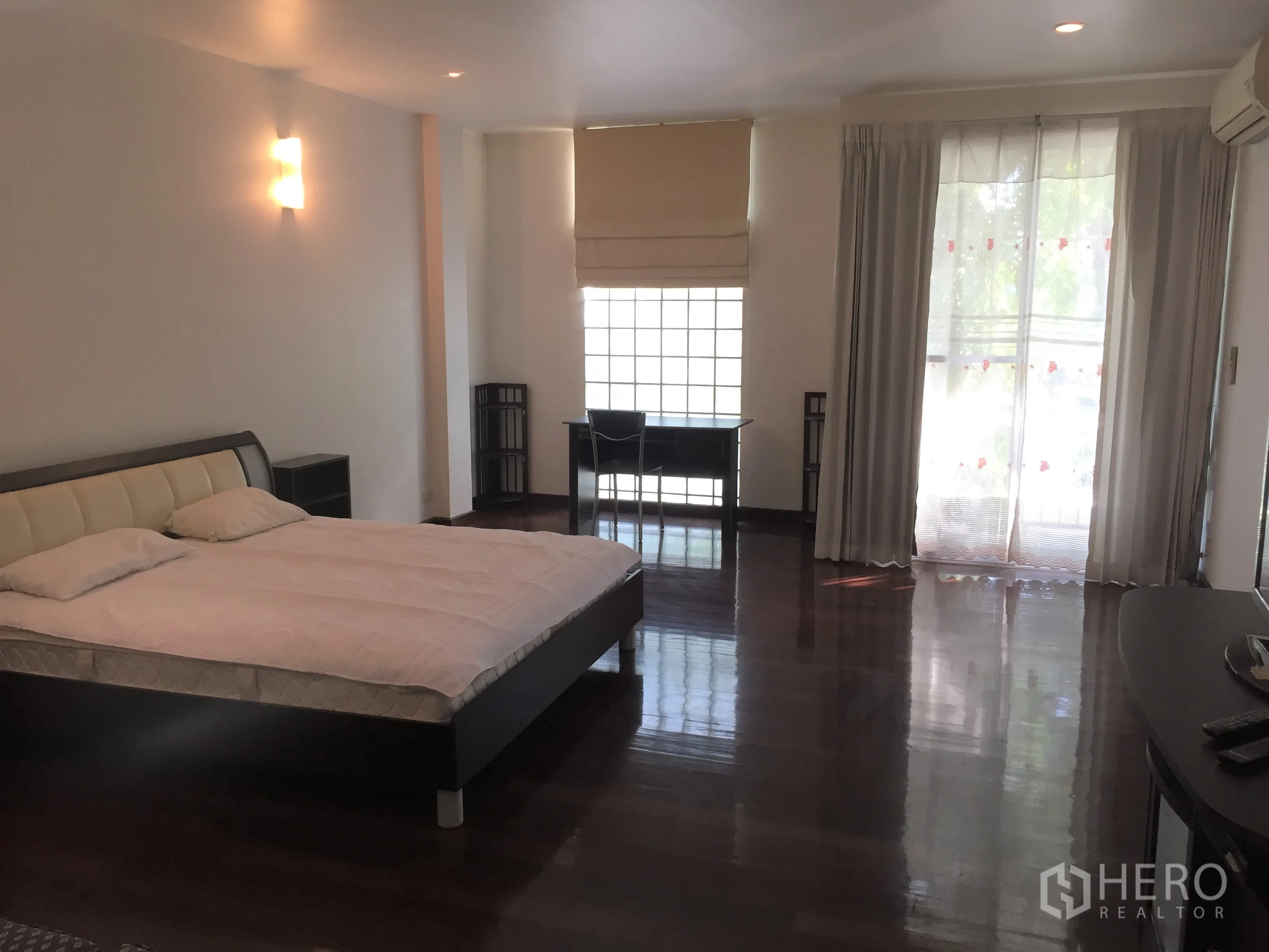 Condominium for rent in Watthana, Bangkok - Spacious master bedroom with hardwood floors, a work desk by the window and sliding doors to a balcony.