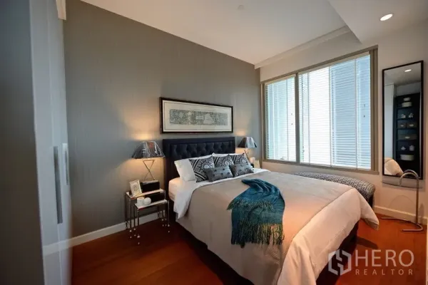 Condominium for rent in Pathum Wan, Bangkok - Cozy bedroom with upholstered headboard, bedside tables and a large window with blinds.