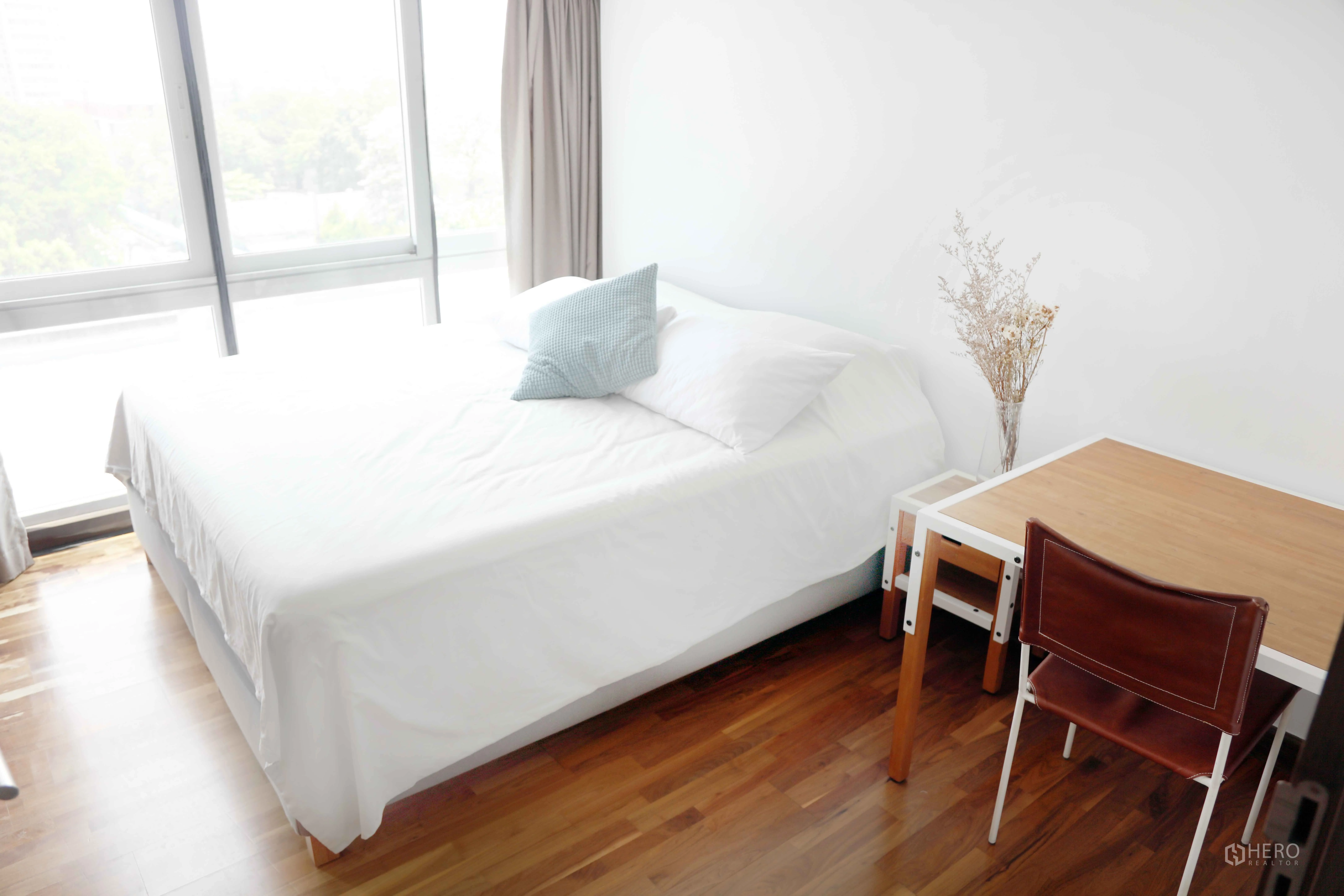 คอนโด for rent in Watthana, Bangkok - ห้องนอนมีหน้าต่างบานใหญ่ เตียงปูผ้าสีขาว และโต๊ะทำงานบนพื้นไม้