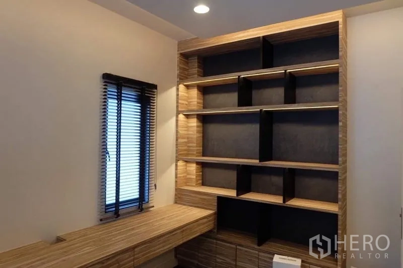 Detached House for rent in Bang Kapi, Bangkok - Compact home office with custom shelving wall, integrated desk and warm accent lighting.