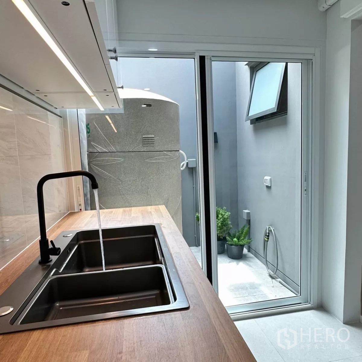 Townhouse for rent in Bang Phli, Samut Prakan - Glossy galley kitchen leading to a sliding door that opens to the service yard and water tank.