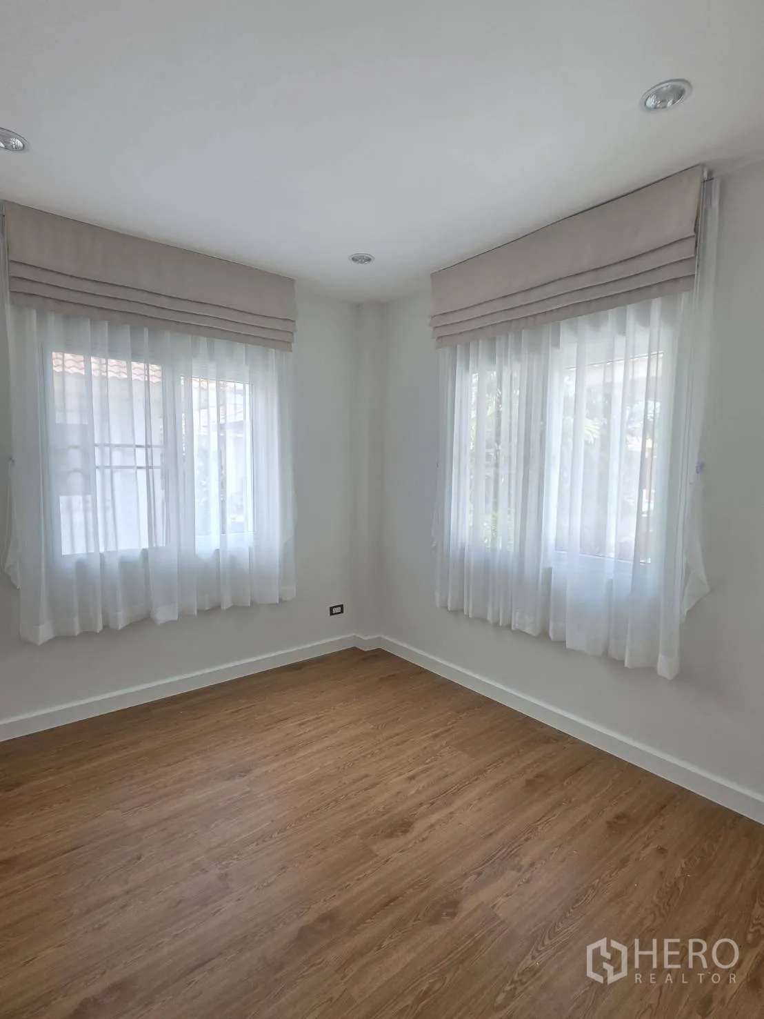 Detached House for sale in Lam Luk Ka, Pathum Thani - Corner bedroom with two windows, sheer curtains, and wood floors.