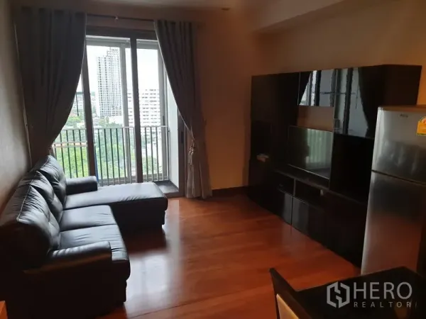 คอนโด ให้เช่าในKhlong Toei, Bangkok - ห้องนั่งเล่นพร้อมโซฟาหนังเข้ามุม ตู้ทีวี และประตูกระจกออกสู่ระเบียงวิวเมือง