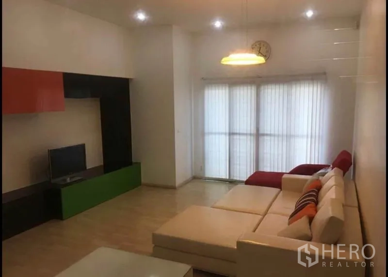 Townhouse for sale in Khlong Toei, Bangkok - Living area with TV wall unit and sectional sofa facing full-height windows.