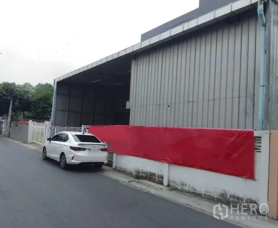 Warehouse for rent in Huai Khwang, Bangkok - Street-side view of a corrugated metal warehouse with a covered loading bay and gated wall in Huai Khwang, Bangkok.