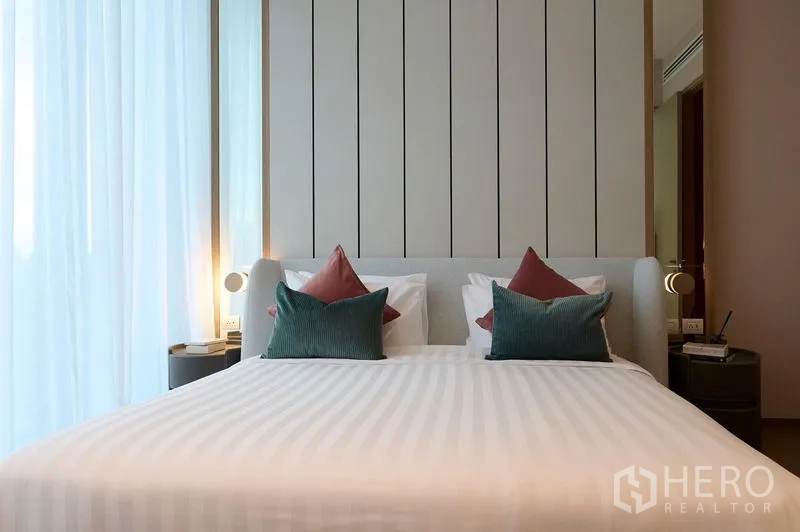 Condominium for rent in Pathum Wan, Bangkok - Close-up of upholstered bed with decorative pillows and warm bedside lighting.