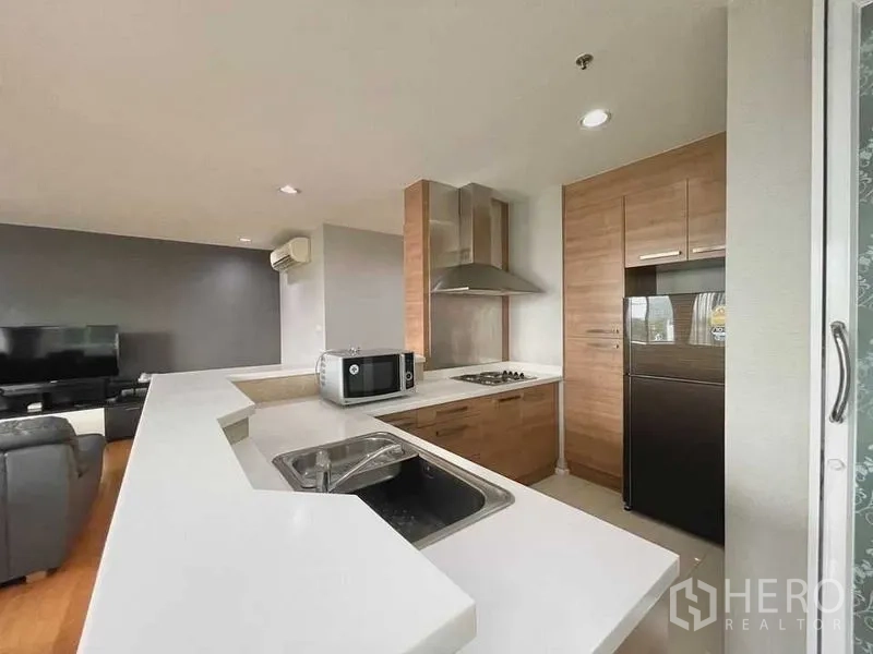 公寓 出租在Watthana, Bangkok - U形厨房配白色台面、水槽、炉灶、油烟机、烤箱、微波炉与冰箱。