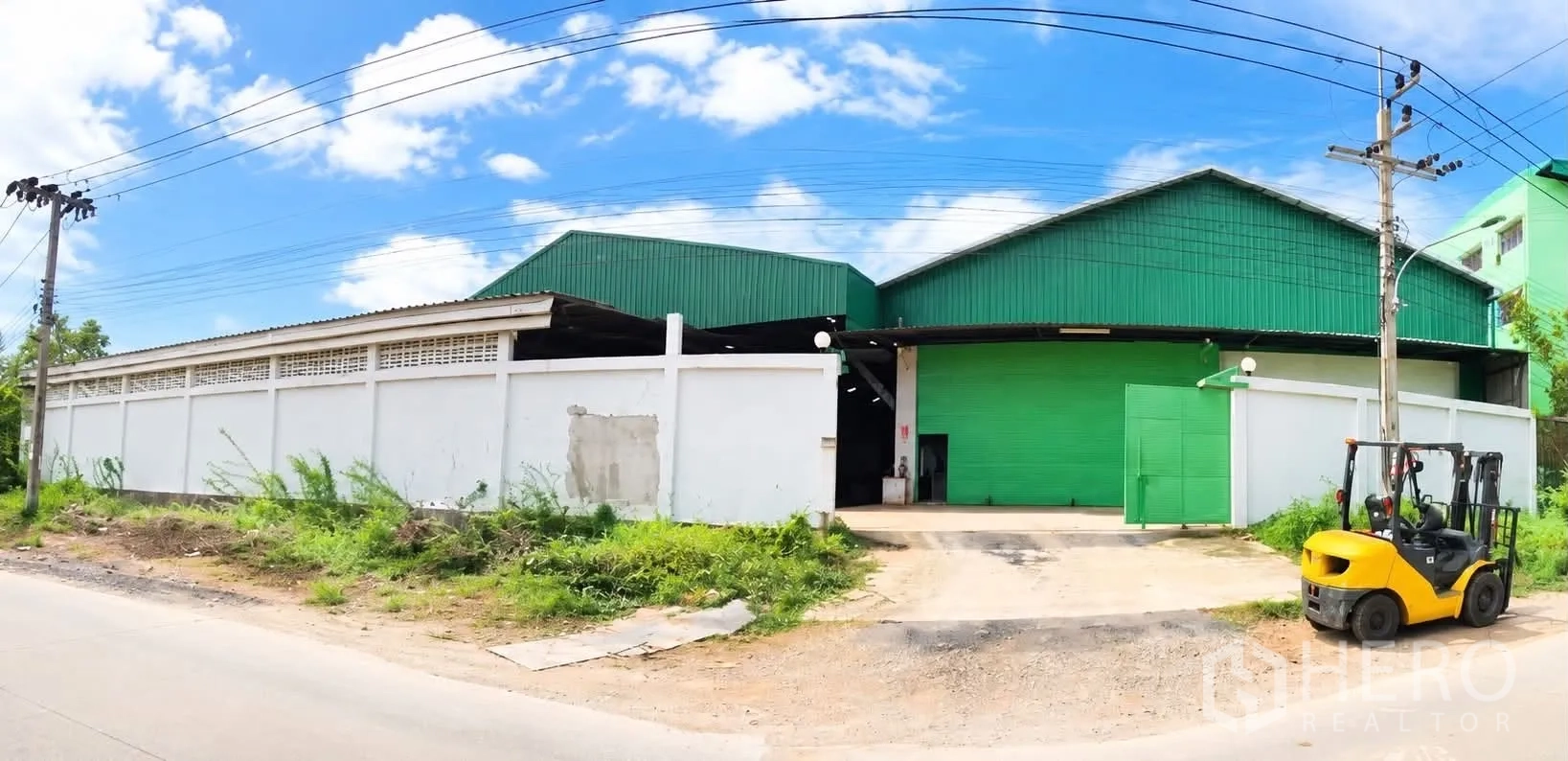Warehouse for rent or sale - Warehouse exterior with roller shutter entrance, perimeter wall, and gated access from the road.