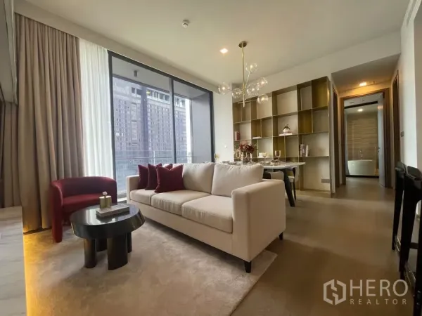 Condominium for rent in Watthana, Bangkok - Bright living room with cream sofa, red armchair, floor-to-ceiling windows and built-in shelving at Celes Asoke.