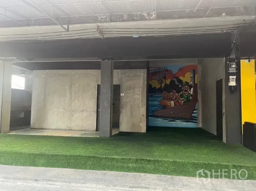 零售空间 出租在Watthana, Bangkok - 临街店铺开口，混凝土墙与人造草坪地面，金属雨棚下带彩色壁画