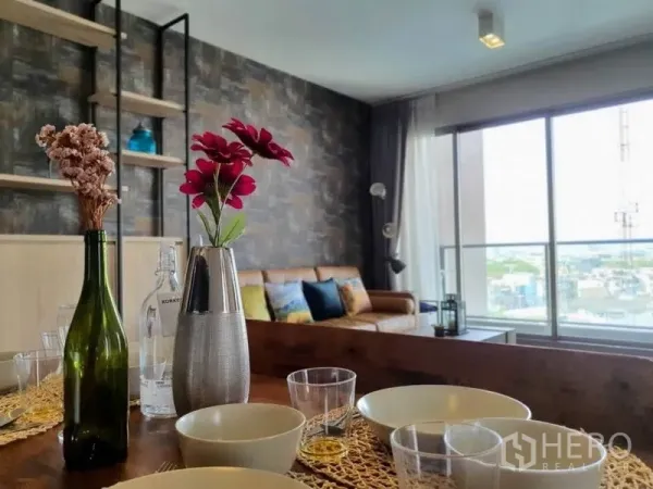 Condominium for rent or sale in Watthana, Bangkok - Dining table with flowers facing a sofa and large windows with city views.