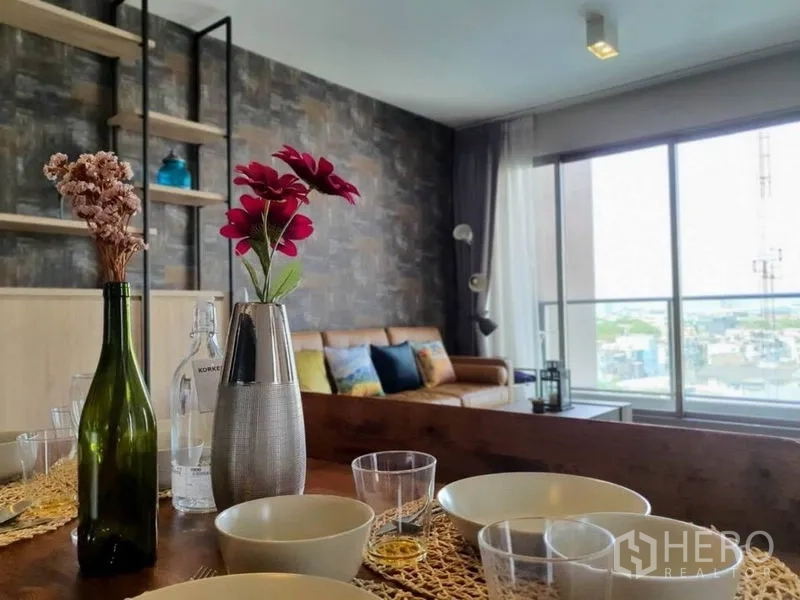 Condominium for rent or sale in Watthana, Bangkok - Dining table with flowers facing a sofa and large windows with city views.