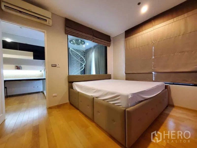 คอนโด ให้เช่าหรือขายในRatchathewi, Bangkok - ห้องนอนปูพื้นไม้ เตียงขนาดใหญ่ มองเห็นโถงโคมระย้าผ่านช่องหน้าต่าง