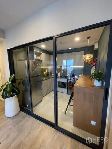 คอนโด ขาย - ครัวกั้นสัดส่วนด้วยประตูกระจกบานสไลด์กรอบดำ ติดกับห้องนั่งเล่น