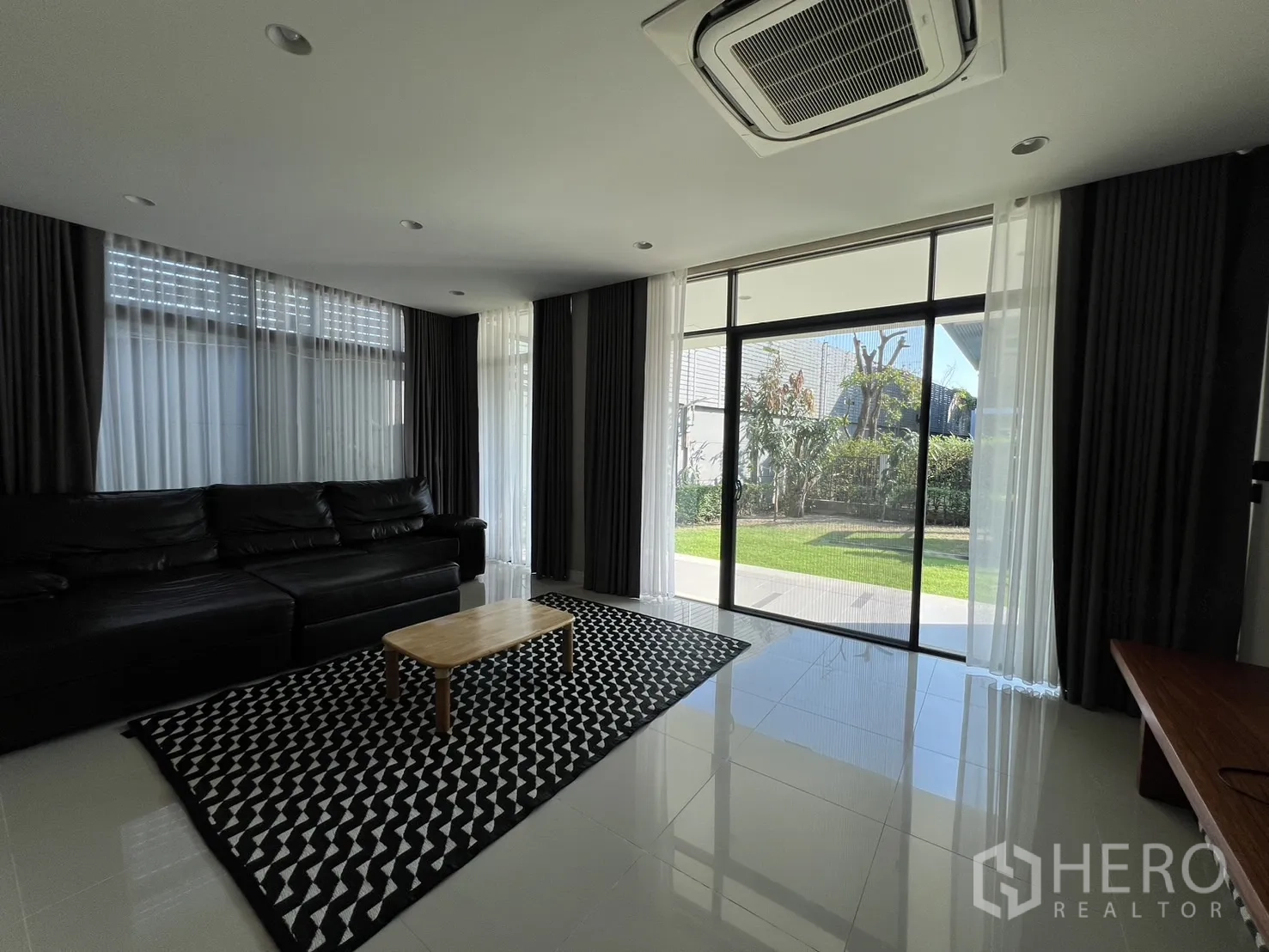 Detached House for rent or sale in Bang Kapi, Bangkok - Bright living room with large sliding doors, black leather sofa and garden outlook.