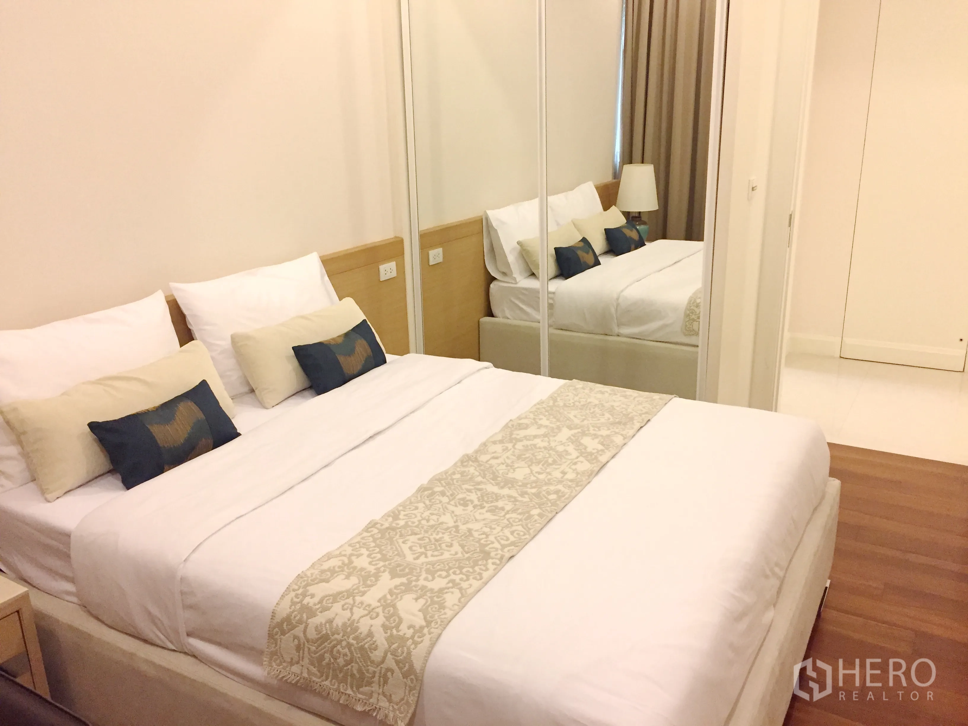 Condominium for rent in Pathum Wan, Bangkok - Bedroom with mirrored wardrobe doors, soft bedding and wood flooring.