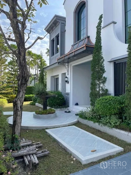 Detached House for sale in Saphan Sung, Bangkok - Front garden and façade with arched windows and manicured shrubs.