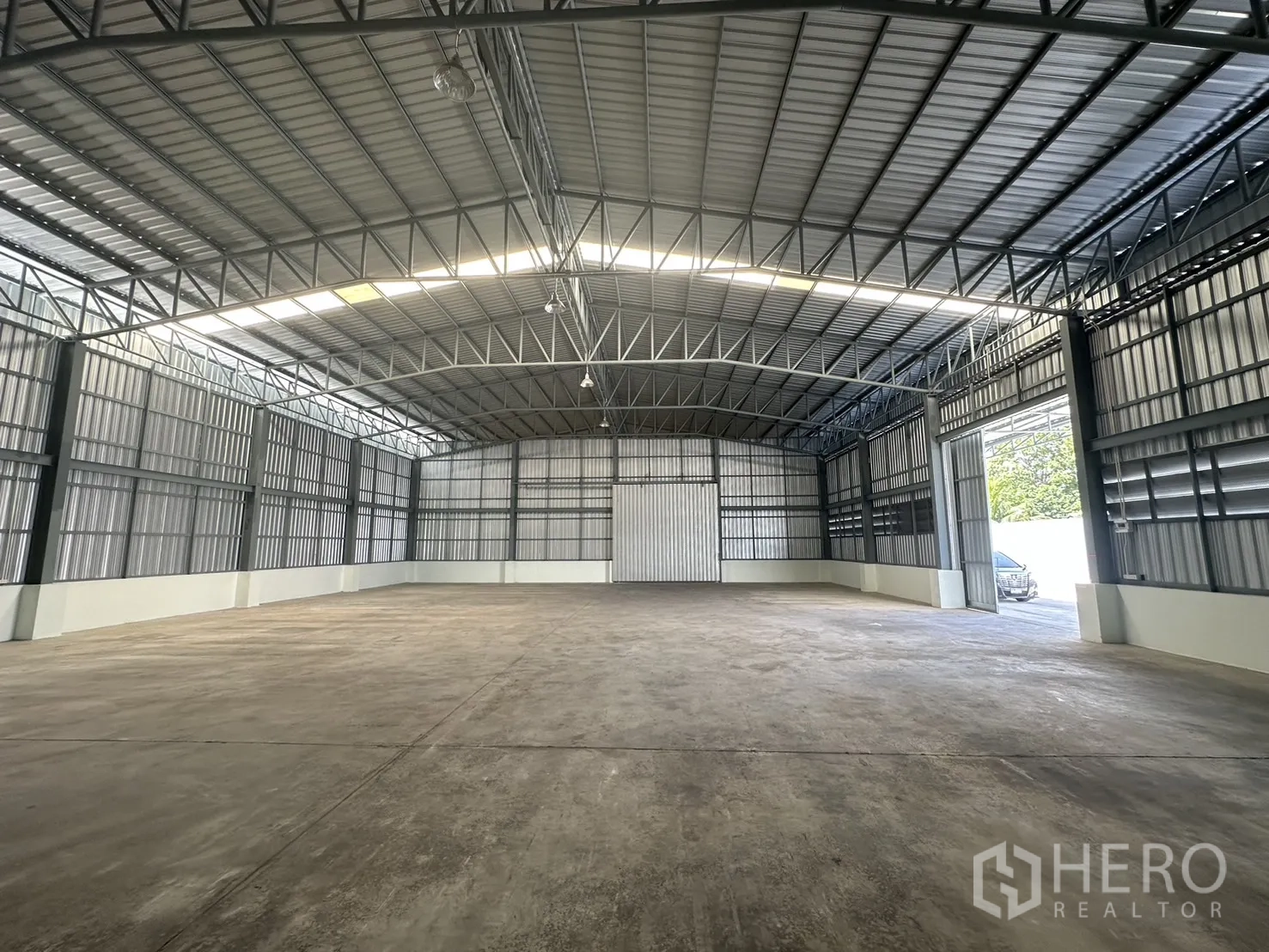 Warehouse for rent in Mueang Pathum Thani, Pathum Thani - Interior looking toward the entrance with large sliding doors, metal walls and high-bay lighting.