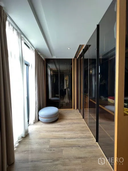 联排别墅 出租在Saphan Sung, Bangkok - 步入式衣帽间走廊，玻璃衣柜与自然采光，配圆形脚凳。