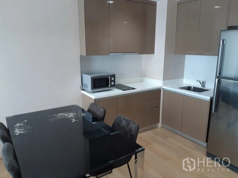 คอนโด ให้เช่าในKhlong Toei, Bangkok - ครัวคอนโดสมัยใหม่ ตู้บานเงา ไมโครเวฟ เตาไฟฟ้า อ่างล้างจาน ตู้เย็น และโต๊ะกินข้าวกระจกสีดำ