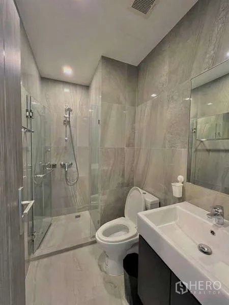 Condominium for sale in Watthana, Bangkok - Modern bathroom with glass shower, gray tiles, vanity and toilet.
