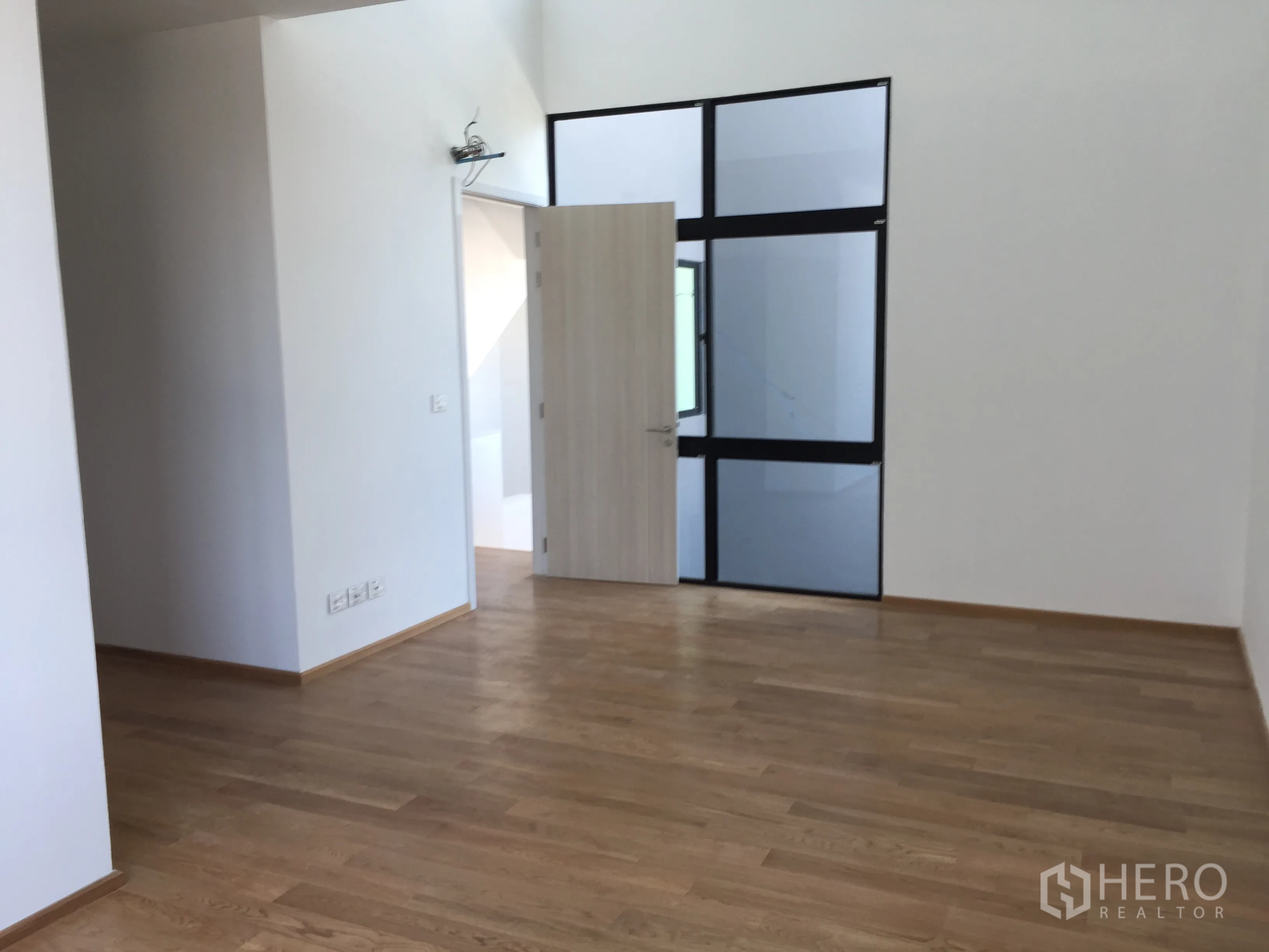 Townhouse for rent in Saphan Sung, Bangkok - Spacious bedroom with light wood flooring and a black-frame interior window.