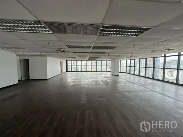 Office Space for rent - Large open-plan office floor with grid ceiling, dark wood flooring and skyline views through wraparound windows.