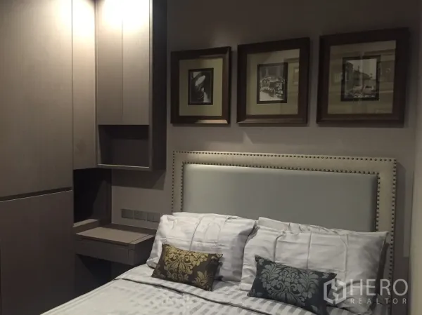 Condominium for rent in Bang Rak, Bangkok - Cozy bedroom with upholstered headboard, built-in wardrobe, and a series of framed artworks above the bed.