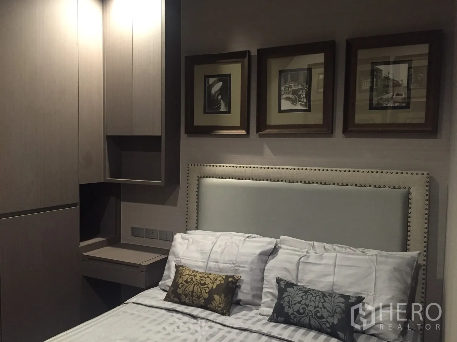 Condominium for rent in Bang Rak, Bangkok - Cozy bedroom with upholstered headboard, built-in wardrobe, and a series of framed artworks above the bed.