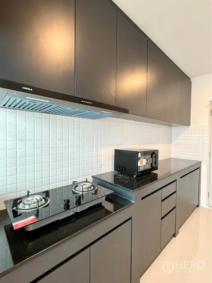 Detached House for rent in Bang Phli, Samut Prakan - Close-up of gas hob, range hood, and microwave on black countertop.