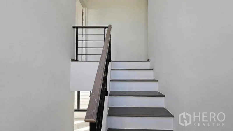 Detached House for sale in Samut Prakan - Tree-lined street view of modern two-storey houses in a gated community.