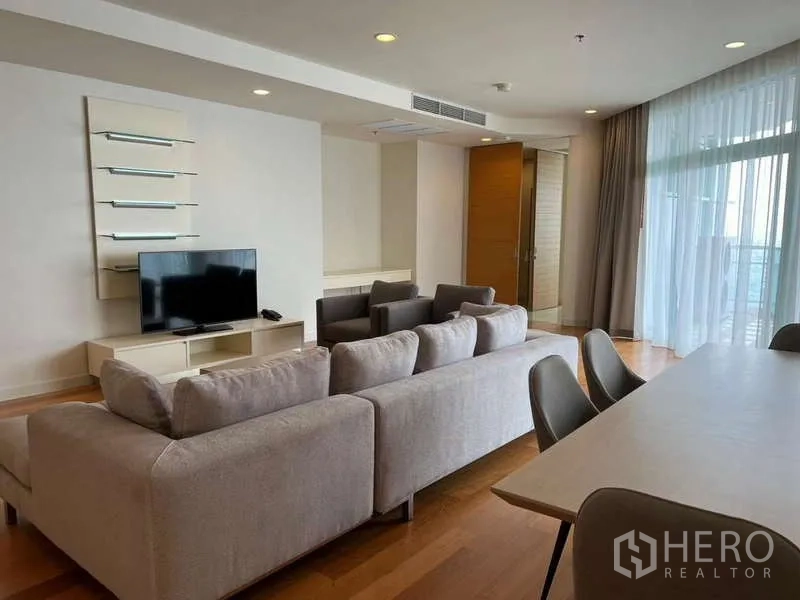 Condominium for rent in Bang Kho Laem, Bangkok - Living room view toward TV and dining table beside balcony doors.