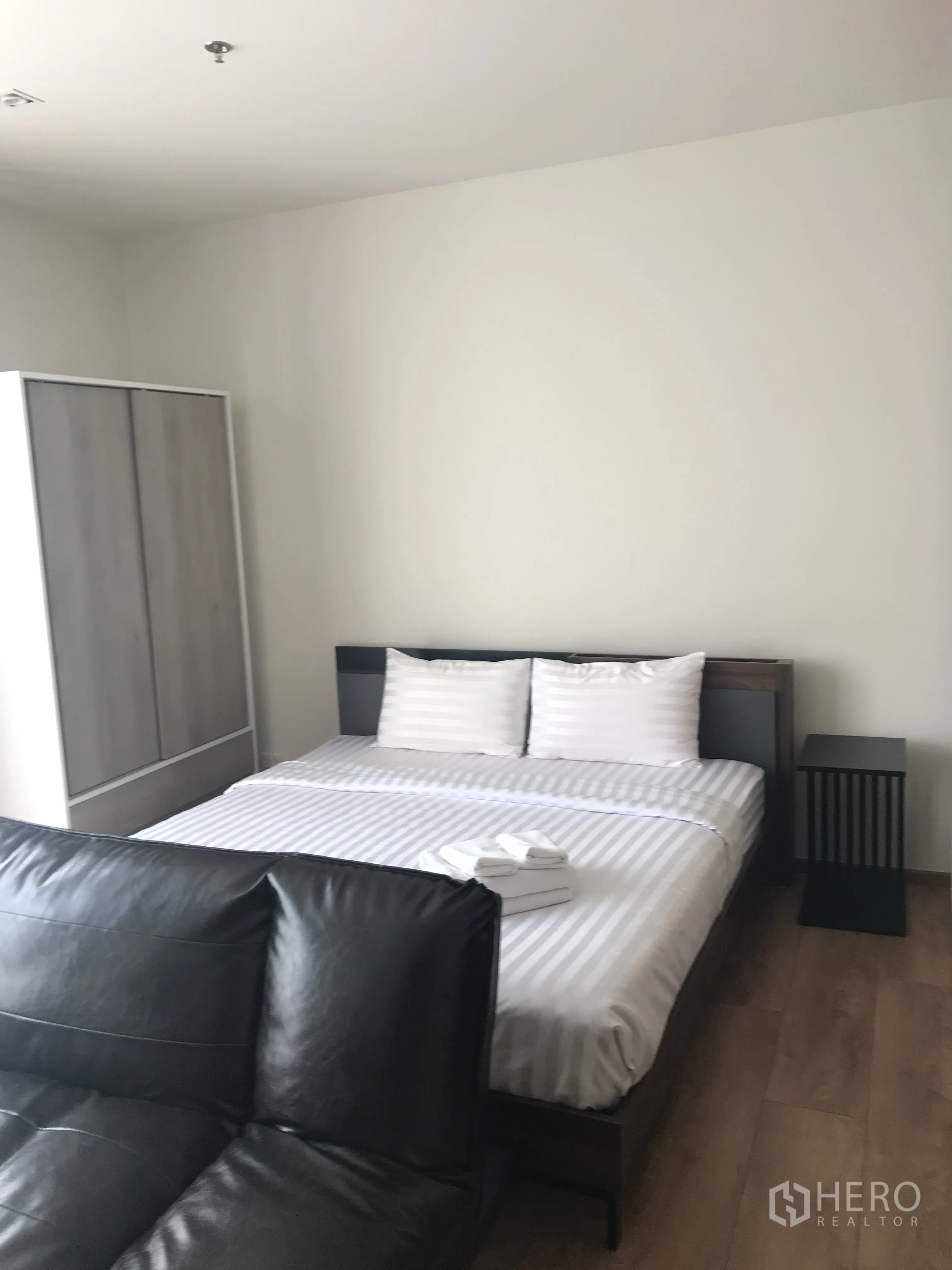 Condominium for sale in Khlong Toei, Bangkok - Spacious room showing bed, bedside table, wardrobe, and sofa.