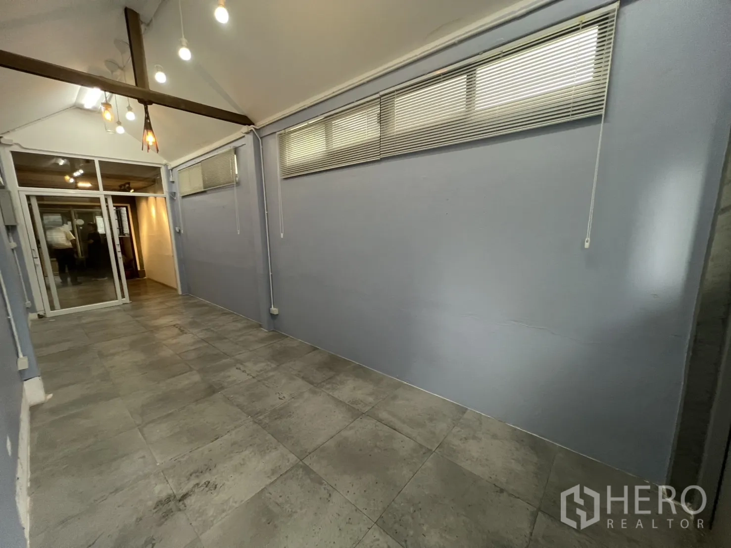 พื้นที่ขายปลีก ให้เช่า - ห้องค้าปลีกทรงยาว พื้นกระเบื้องสีเทา ผนังสีฟ้า และประตูกระจกบานเลื่อน