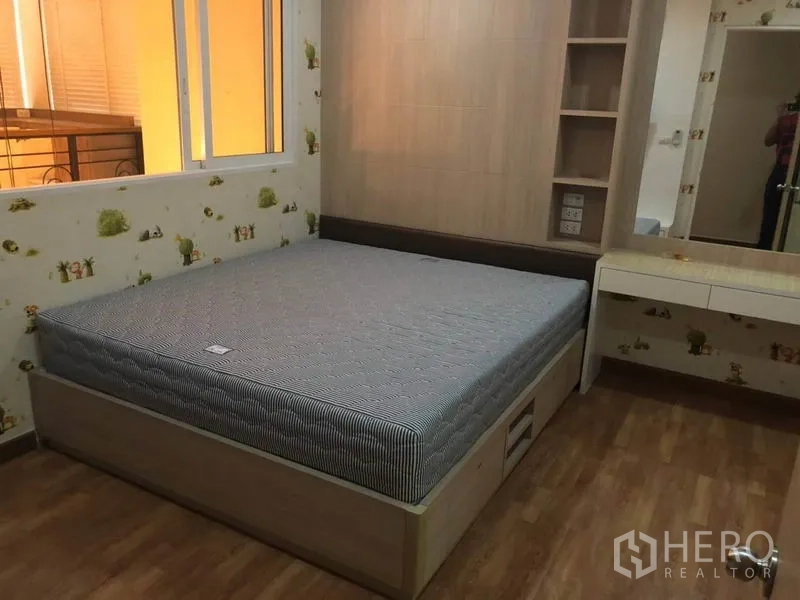 Condominium for sale in Bang Na, Bangkok - Bedroom with built-in headboard, storage shelves, dressing table and wood flooring.