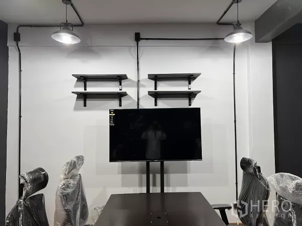 Home Office for rent in Pom Prap Sattru Phai, Bangkok - Wall with floating shelves and a mounted TV beneath exposed conduit lights in a meeting area.