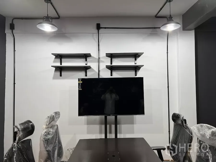 Home Office for rent in Pom Prap Sattru Phai, Bangkok - Wall with floating shelves and a mounted TV beneath exposed conduit lights in a meeting area.