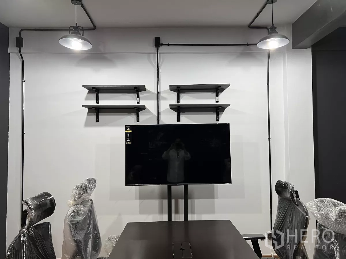 Home Office for rent in Pom Prap Sattru Phai, Bangkok - Wall with floating shelves and a mounted TV beneath exposed conduit lights in a meeting area.
