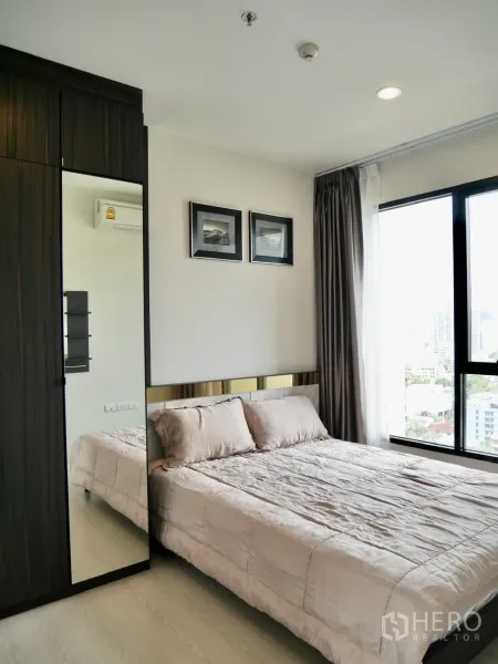 Condominium for rent in Pathum Wan, Bangkok - Cozy bedroom with large window, built-in wardrobe and neutral bedding.