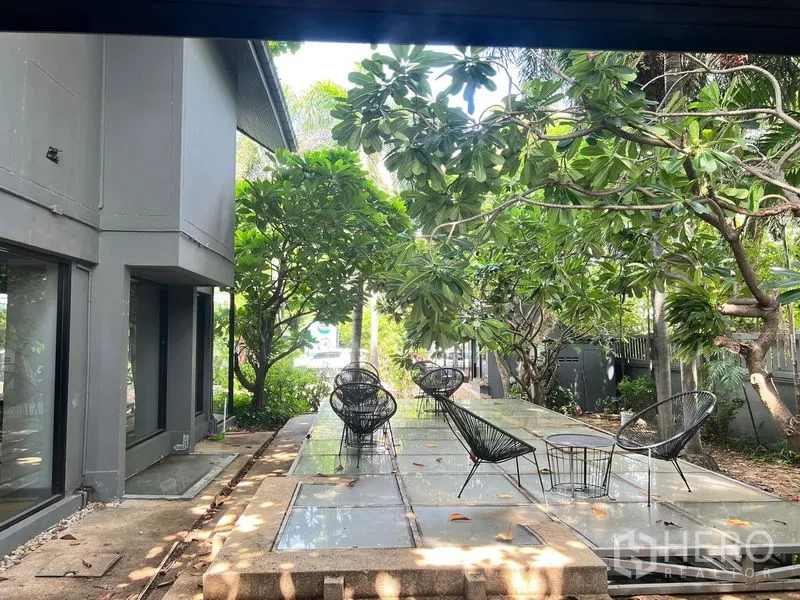 零售空间 出租在Bangkok - 花园露台座位，灰色建筑旁环绕成熟热带树木。