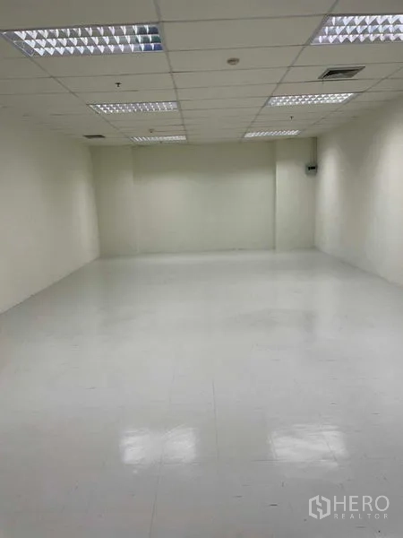 办公空间 出租在Watthana, Bangkok - 开放式白色办公室，亮面地砖、吊顶网格与明亮荧光灯。