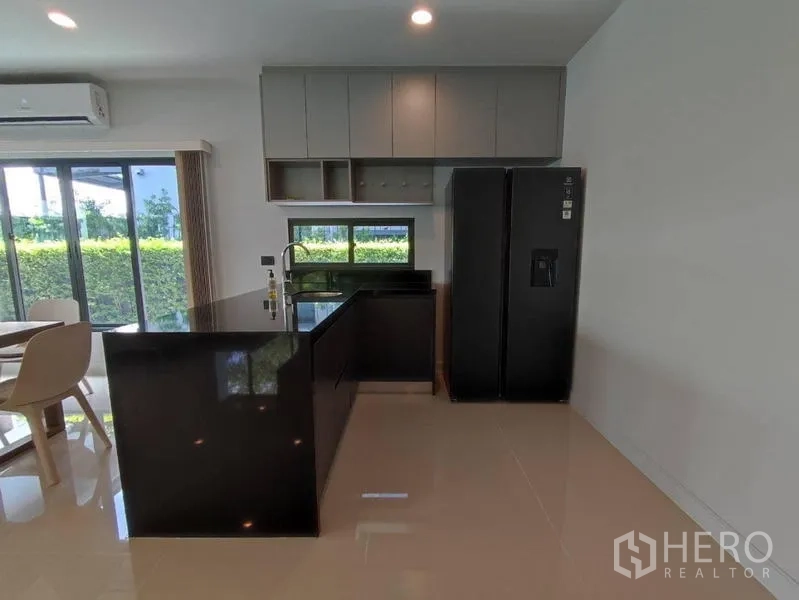 Detached House for rent in Bang Kapi, Bangkok - Full kitchen view showing peninsula counter, upper cabinets and garden outlook through windows.