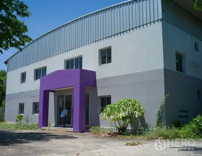 工厂 出租在Pathum Thani - 现代工厂外立面，紫色门廊与玻璃门，前方有硬化院落。