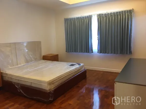 Detached House for rent in Watthana, Bangkok - Guest bedroom with wooden flooring, double windows with blue curtains and bedside tables.