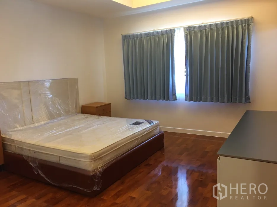 Detached House for rent in Watthana, Bangkok - Guest bedroom with wooden flooring, double windows with blue curtains and bedside tables.